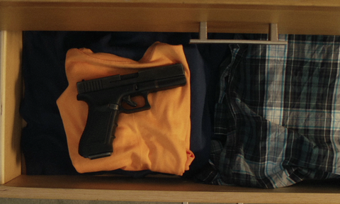 An unsecured gun in an open drawer with clothes